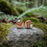 clous-oreilles-bois-indyana-couleur-1 Deux boucles d'oreilles en bois avec accents gris-bleu, motifs géométriques, sur pierre mouillée couverte de mousse verte