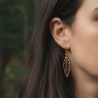 Ekinox-Ohrring aus Holz mit Schweizer Holzblattanhänger, getragen am Ohr einer Frau mit schwarzem Haar und verschwommenem grünem Laub im Hintergrund