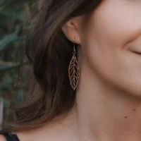 Ekinox-Ohrring aus Holz mit einem Anhänger in Form eines Schweizer Holzblatts, getragen am Ohr einer Frau mit langem, schwarzem Haar