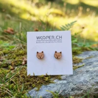 Orecchini a bottone in legno - Rox fox - 3 Orecchini in legno incisi a forma di teste di volpe, su una scheda di presentazione Wooper, posizionati in un ambiente naturale con muschio, foglie e felci