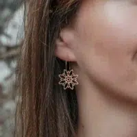 Boucles-oreilles-en-bois-edelweiss-2 Boucles d'oreilles en bois au design d'Edelweiss avec anneaux dorés portés par une femme