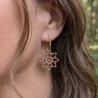 Boucles-oreilles-en-bois-edelweiss Boucles d'oreilles en bois au design d'Edelweiss avec anneaux dorés portés par une femme